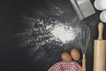 The eggs with a cup of flour and whisk on the black table spread of flour