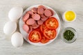 Eggs, slices of sausages and tomato in plate, salt shaker, bowl with parsley on wooden table. Top view Royalty Free Stock Photo