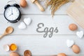 Eggs text letter on white kitchen table with fresh raw eggs, yellow yolk eggs, white heart shape sign and classic vintage clock. Royalty Free Stock Photo