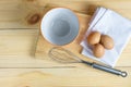 Eggs with whisk and empty orange bowl on wooden plate