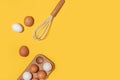 Eggs in wooden egg box and whisk on yellow background. Flat lay Top view Copy space Royalty Free Stock Photo