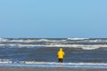 a fisherman with a yellow cagoule standing in the rough sea of the North sea close to the beach Royalty Free Stock Photo