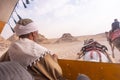 Egyptian driving the chariot near Pyramids through the desert following tourists on camels