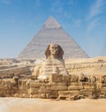 Egyptian Great Sphinx full body portrait with head, feet with all pyramids of Menkaure, Khafre, Khufu in background on a Royalty Free Stock Photo