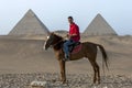 An Egyptian man sits on his horse in front of The Pyramid of Khafre and the Pyramid of Khufu in Giza in Cairo, Egypt.