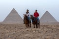 Egyptian men sit on their horses infront of The Pyramid of Khafre and the Pyramid of Khufu in Egypt.