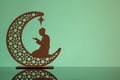 Eid Mubarak concepts with crescent moon in silhouette with man praying.