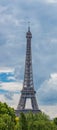 Eiffel Tower behind the trees against the backdrop of a bright cloudy sky Royalty Free Stock Photo