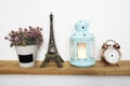 Eiffel tower statue, artificial plant, vintage alarm clock and blue lantern with LED candle light on wooden shelves Royalty Free Stock Photo