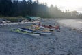 Eight colourful sea kayaks on a sandy beach with a shelter and tents behind