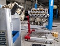 An eight-cylinder iron engine removed from a car near a blue lift in service on a red stand against a background of wrenches and