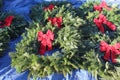 Eight natural Christmas wreaths decorated with red bows lying on a tarp.