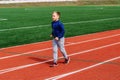 Eight-year-old Caucasian boy in sports uniform runs on the red treadmill at the stadium
