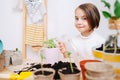 Eight year old girl in warm long spraying seedling on a table in a pot