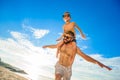 Eight years old boy sitting on dad`s shoulders. Both in swimming shorts and sunglasses, having fun on the beach. Bottom view