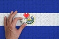 El Salvador flag is depicted on a puzzle, which the man`s hand completes to fold