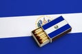 El Salvador flag is shown in an open matchbox, which is filled with matches and lies on a large flag