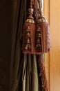 Elaborate large window curtain tie back tassels, cords, and trim over green silk curtains, warm wood background
