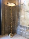 Tall brass light stand with marble wall and floor.