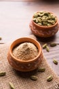 Cardamom powder or elaichi powder in bowl over moody background with pods.