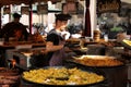 A young cook dressed in black, is serving a plate of tasty paella at a street stall of a medieval fair.