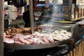 A close up of a wide variety of tasty sausage portions and pork and beef meat is being cooked.