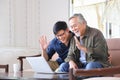 Elder Asian man and his son using video call from computer to say hi to the rest of his family in his cozy retirement home Royalty Free Stock Photo