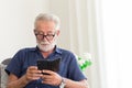 Elder gray beard white hair with glasses looking attention at his smartphone to reading news at home alone