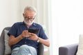 Elder gray beard white hair with glasses looking attention at his smartphone to reading news at home alone