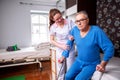 Elder man in nursing home holding a crutch under his arm while nursing home lady is assisting him with standing up Royalty Free Stock Photo