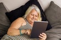 An elder obese woman laying on the bed looks at a tablet Royalty Free Stock Photo