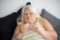 Elder obese woman sitting down on the bed while eating candy Royalty Free Stock Photo