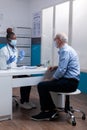 Elder patient sitting at desk getting medical advice from black medic