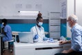 Elder patient sitting at desk getting medical advice from black medic