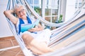 Elder senior woman with grey hair smiling happy relaxing on a hammock reading a book at home Royalty Free Stock Photo