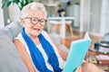 Elder senior woman with grey hair smiling happy sitting on the sofa reading a book at home Royalty Free Stock Photo