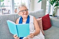 Elder senior woman with grey hair smiling happy sitting on the sofa reading a book at home Royalty Free Stock Photo