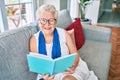 Elder senior woman with grey hair smiling happy sitting on the sofa reading a book at home Royalty Free Stock Photo
