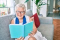 Elder senior woman with grey hair smiling happy sitting on the sofa reading a book at home Royalty Free Stock Photo
