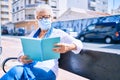 Elder senior woman with grey hair wearing coronavirus safety mask outdoors sitting on a bench reading a book Royalty Free Stock Photo