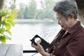 elder woman holding mobile phone in garden. elderly female texting message, using app with smartphone in park. senior use Royalty Free Stock Photo