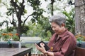 elder woman holding mobile phone in garden. elderly female texting message, using app with smartphone in park. senior use Royalty Free Stock Photo