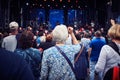 Elder women raising her arm in the crowd and listening to the group on stage at an outdoor music festival