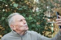 An elderly active handsome man with a mustache takes a selfie with a mobile phone. An elderly man looks at the camera and poses