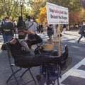 An elderly African American man is sitting next to a banner that says `Stop Hating Each Other Because You Disagree`