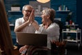 Elderly artist couple holding laptop doing high five hand gesture celebrating selling artwork in online auction Royalty Free Stock Photo