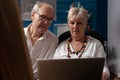 Elderly artist couple holding laptop looking at screen trying to sell artwork in online auction