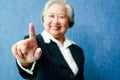 An elderly Asian businesswoman puts her right index finger forward.