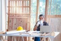 Elderly Asian carpenter with mustache taking a break and drinking a coffee, relaxing senior craftsman setting in working desk at