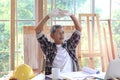 Elderly Asian carpenter with mustache taking a break and drinking a coffee, relaxing senior craftsman setting in working desk at
